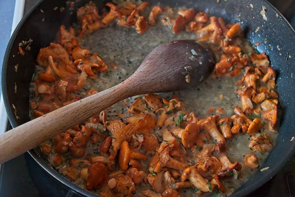 White wine poured into a pan with chanterelles and onions