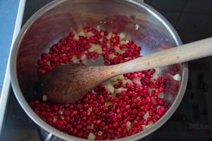 Apples and lingonberries starting to cook together in a saucepan.