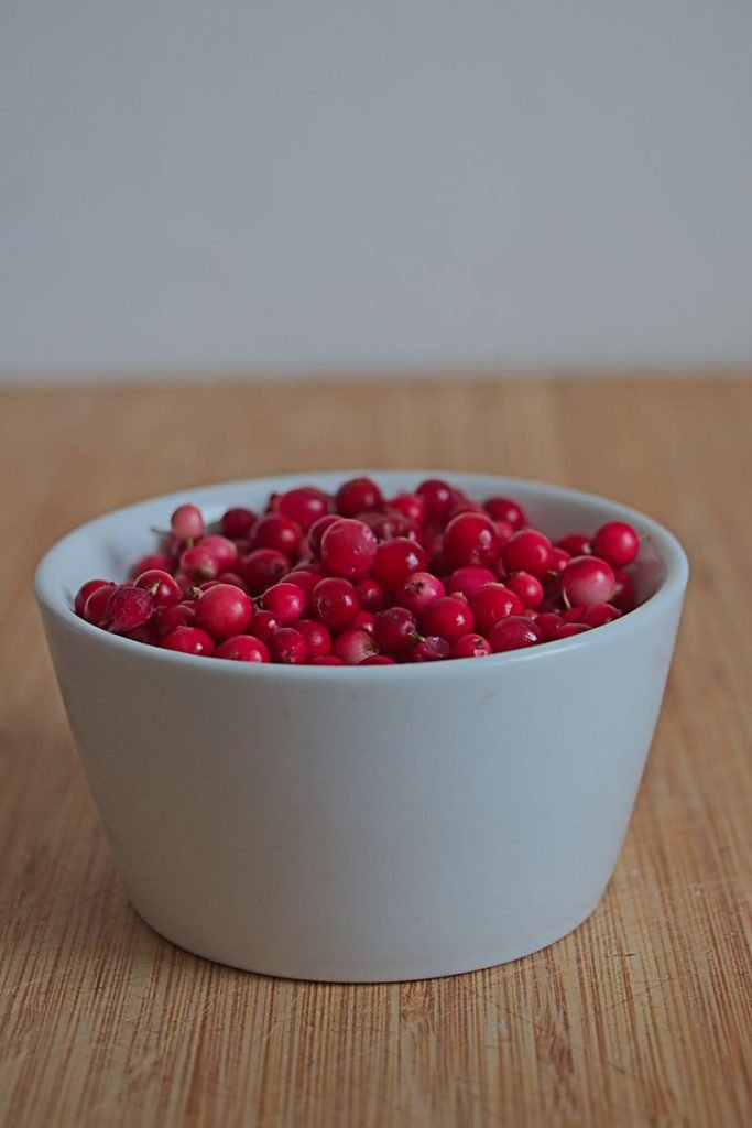 Fresh lingonberries in a white bowl on a wooden table.