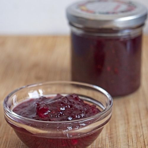Homemade lingonberry apple jam in glass jars, one open and one sealed.
