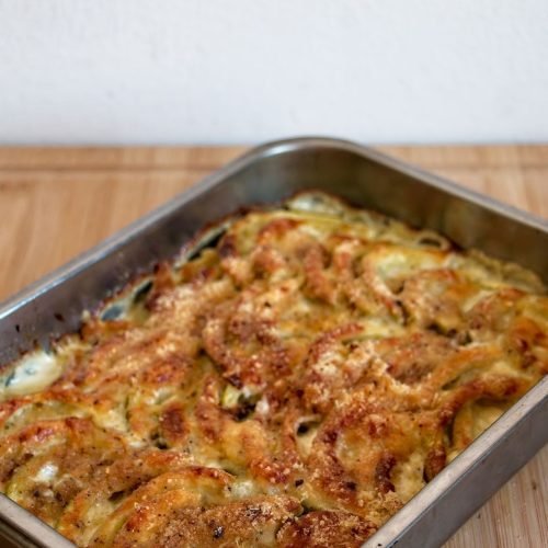 Side view of baked tromboncino gratin in a metal dish with golden cheese topping and crisp edges.