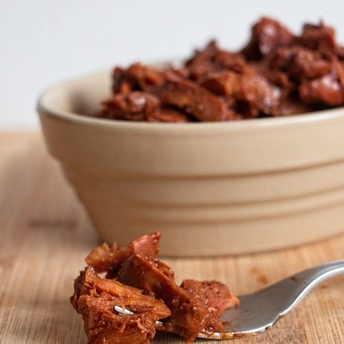 Slow cooker BBQ chicken of the woods in a bowl with a fork, coated in glossy barbecue sauce.