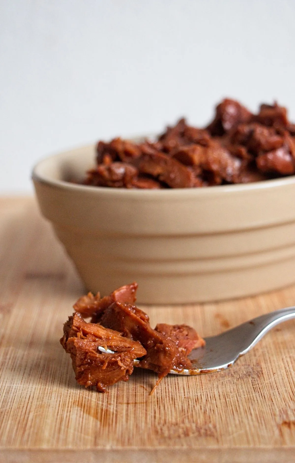 Slow cooker BBQ chicken of the woods in a bowl with a fork, coated in glossy barbecue sauce.