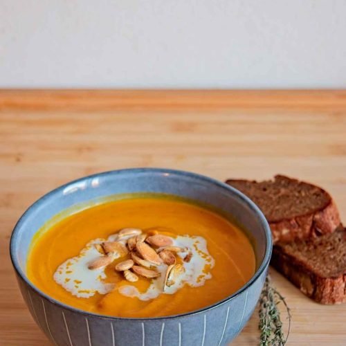 Bowl of honey roasted pumpkin soup with cream, roasted seeds, and bread