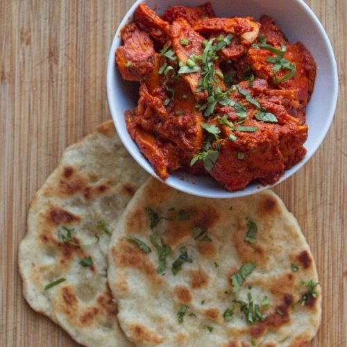 Bowl of chicken of the woods butter chicken served with naan bread and fresh coriander garnish