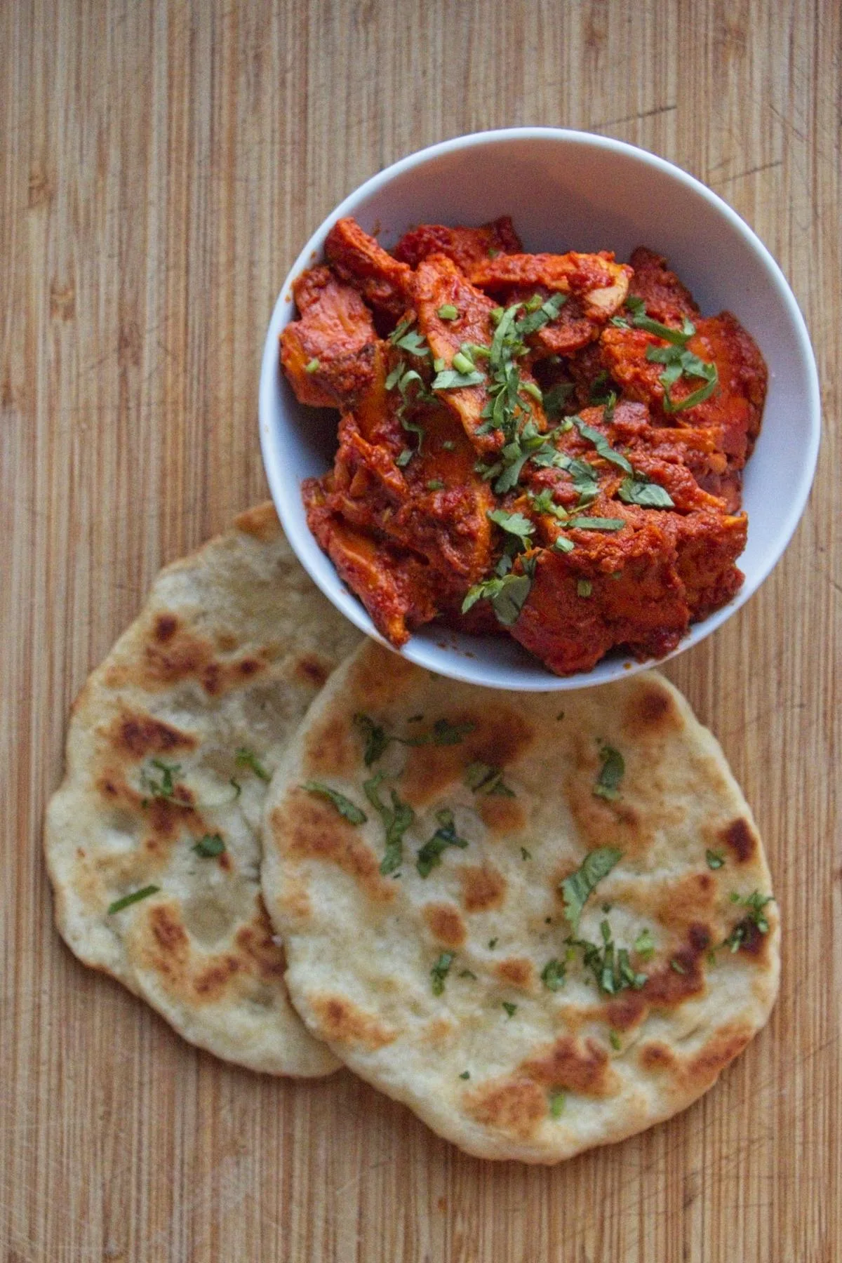 Bowl of chicken of the woods butter chicken served with naan bread and fresh coriander garnish