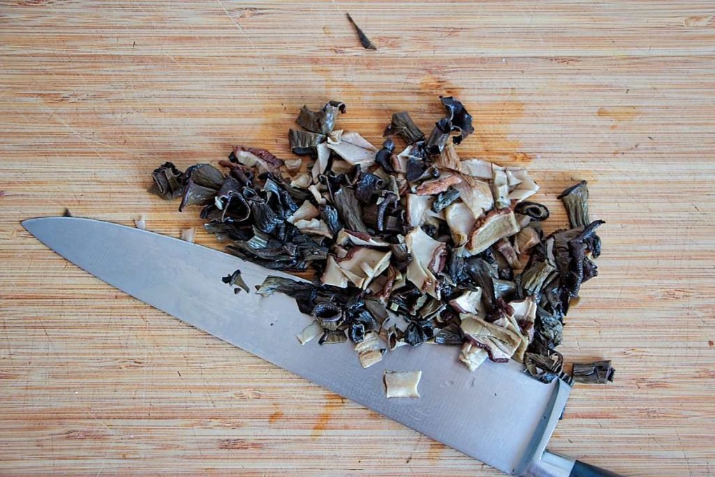 Chopped rehydrated ceps and horn of plenty mushrooms on a cutting board0
