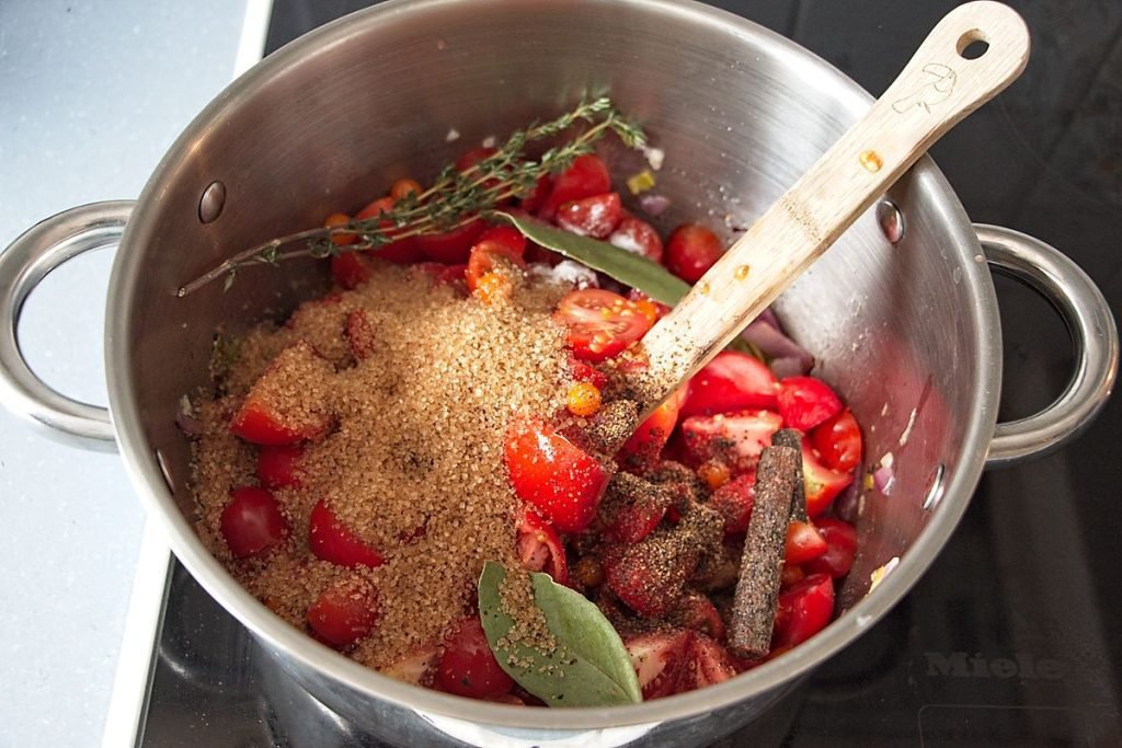 Cooking onions, leek, tomatoes, and spices in a pot for homemade tomato ketchup recipe