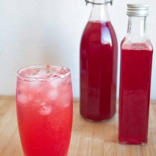 Glass of iced cornelian cherry cordial with two bottles of homemade syrup behind