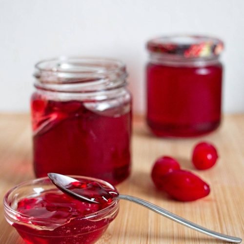 Cornelian cherry jelly jars with spoon and fresh cherries on wooden board