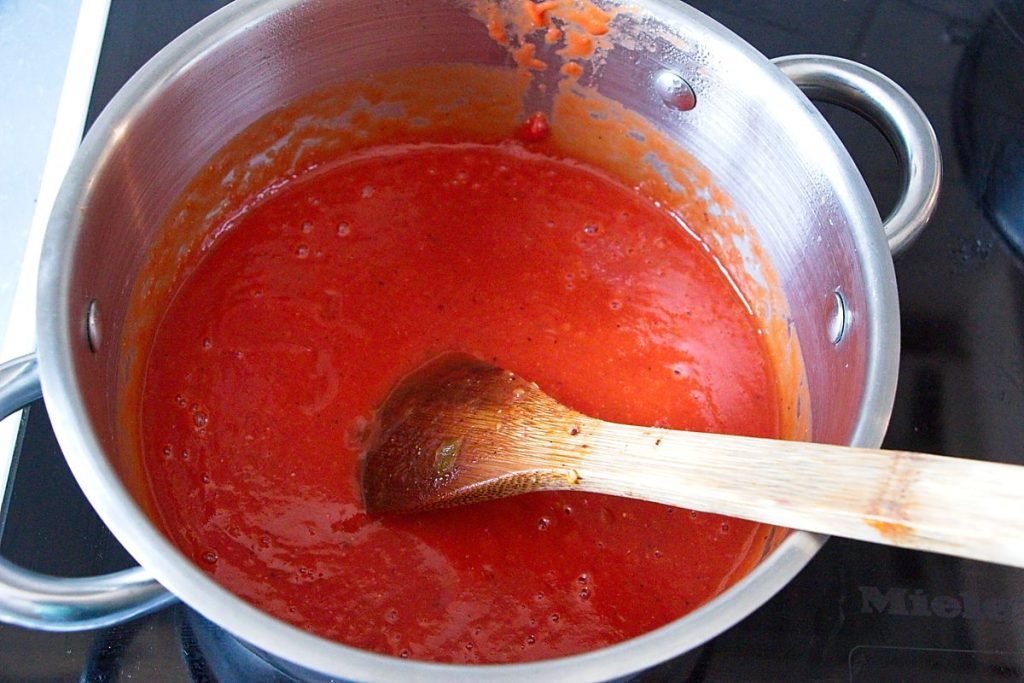 Finished homemade tomato ketchup simmering in a pot with a wooden spoon