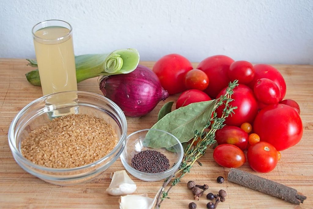 Ingredients for homemade tomato ketchup including tomatoes, red onion, leek, garlic, vinegar, sugar, and spices