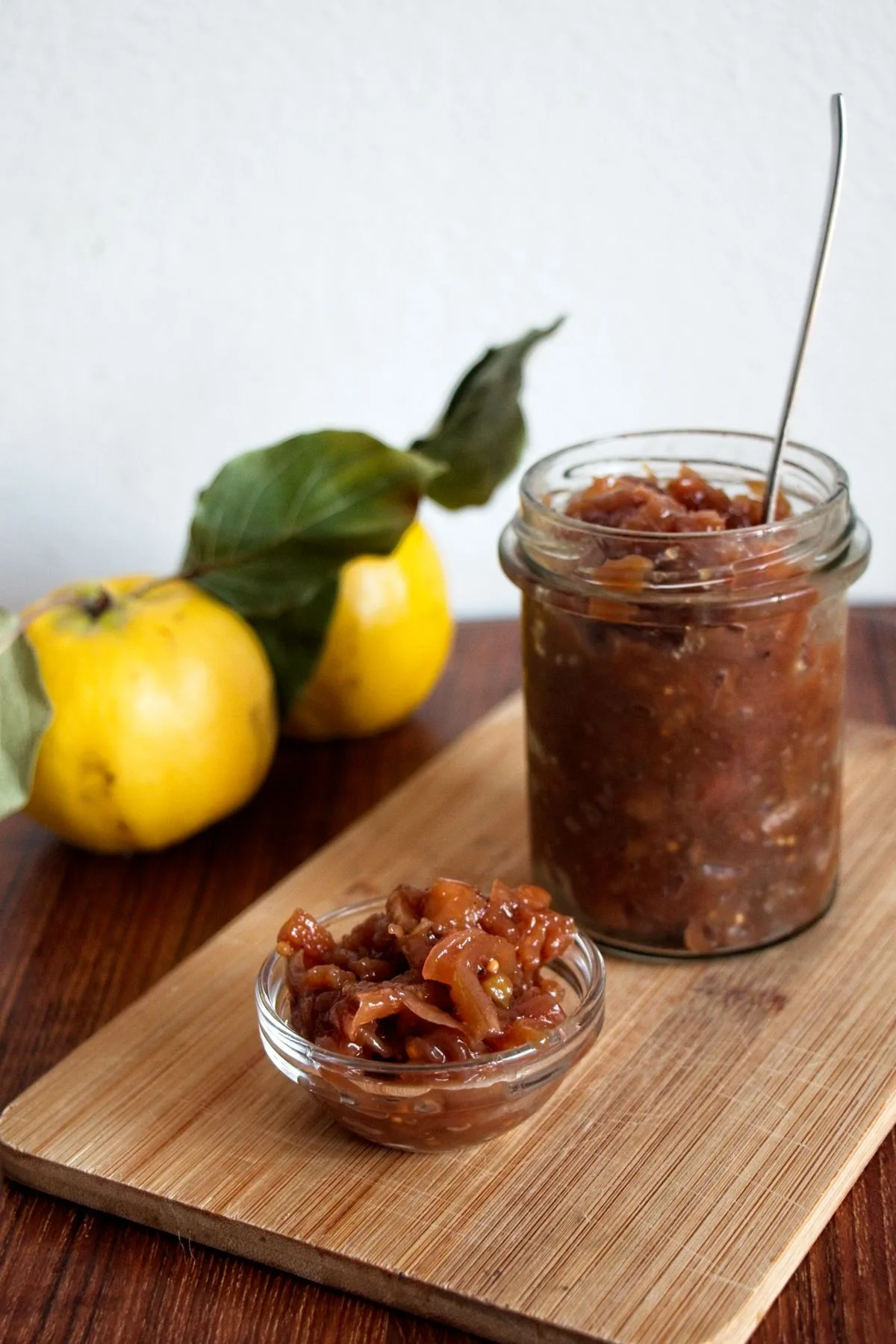 Jar and bowl of homemade Caramelised Onion and Quince Chutney on a wooden board with fresh quinces.