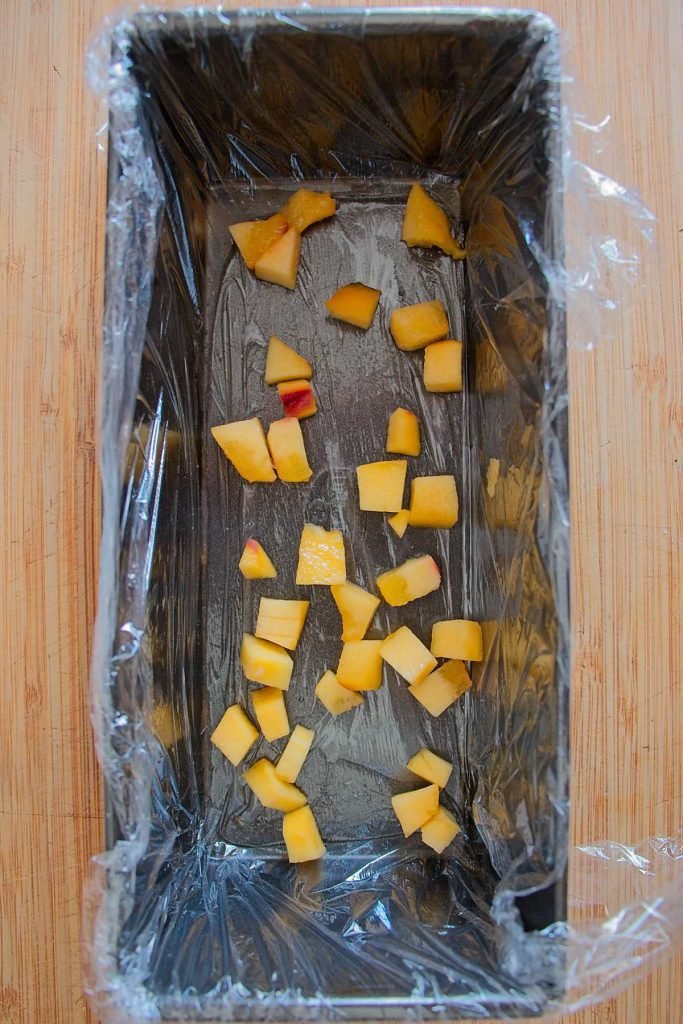 Diced fresh peaches layered in the base of a cling film–lined loaf tin.