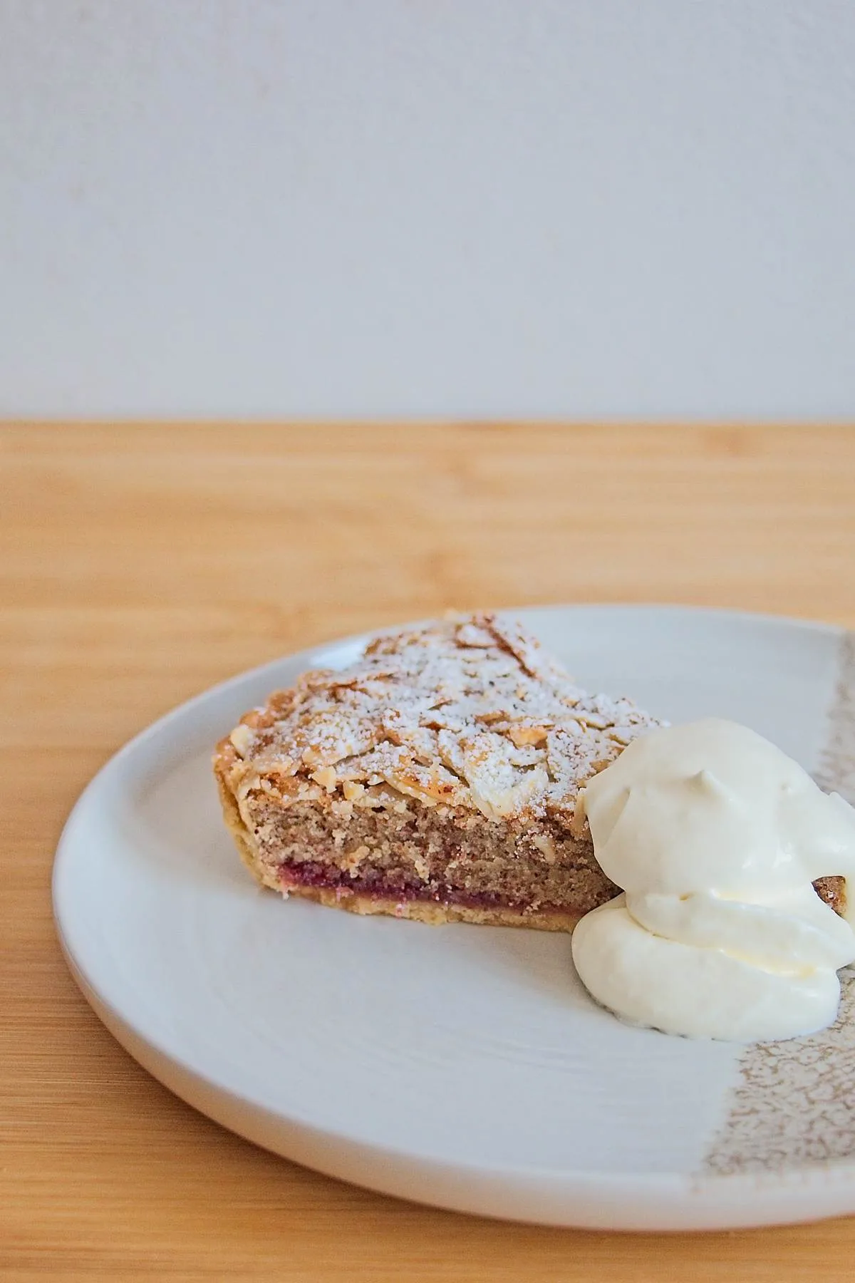 Slice of lingonberry Bakewell tart on a plate, served with whipped cream.