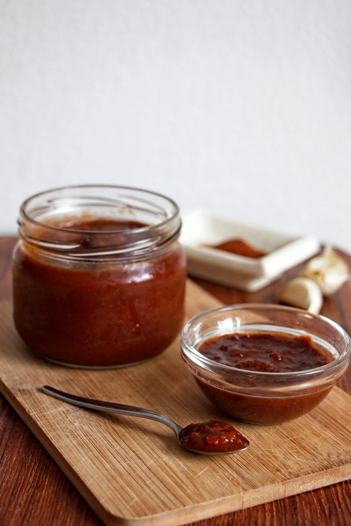 Homemade Cornelian Cherry BBQ Sauce in a jar and bowl with a spoon on a wooden board.