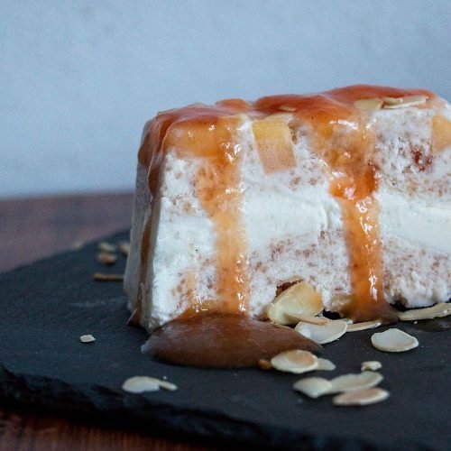 Peach frozen yogurt terrine with cardamom, topped with syrup and toasted almonds, served on slate.