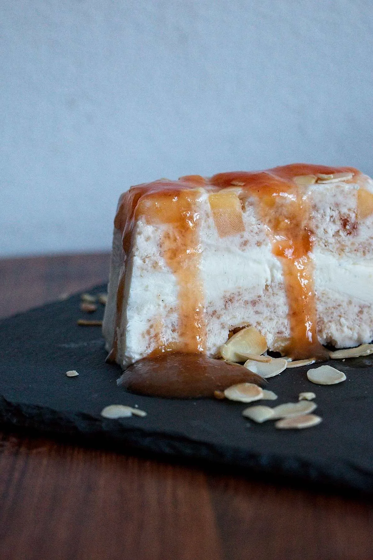 Peach frozen yogurt terrine with cardamom, topped with syrup and toasted almonds, served on slate.