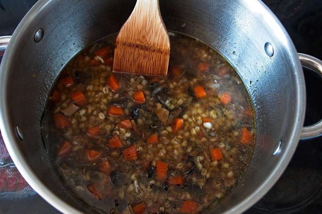 Wheat berry and wild mushroom soup simmering in a pot with carrots and herbs