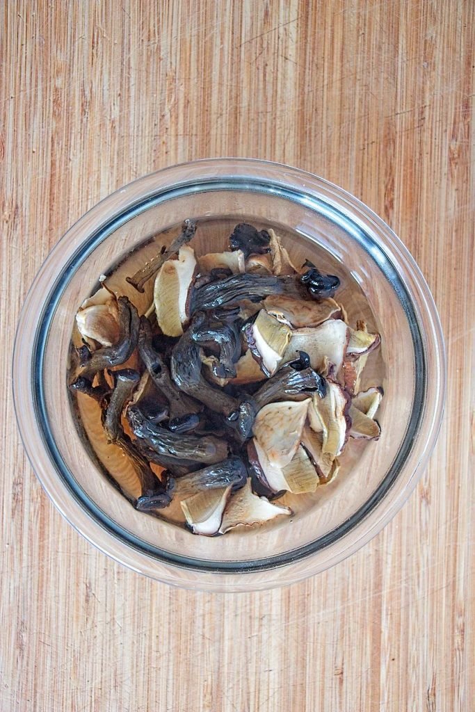 Dried porcini and horn of plenty mushrooms soaking in a glass bowl with hot water