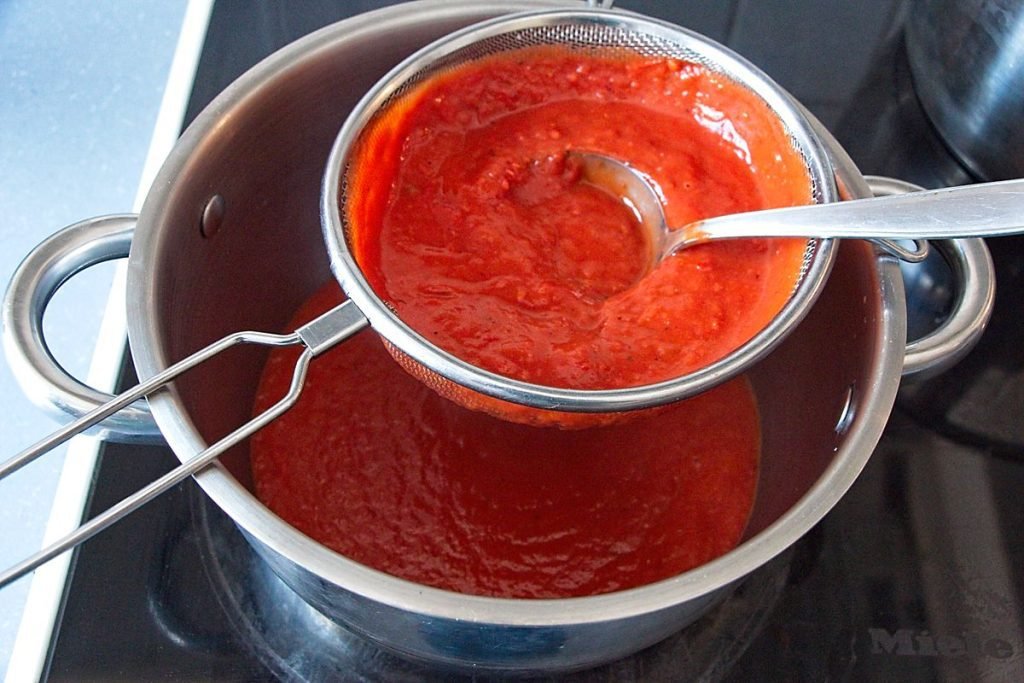 Straining homemade tomato ketchup through a sieve with a ladle for a smooth silky texture