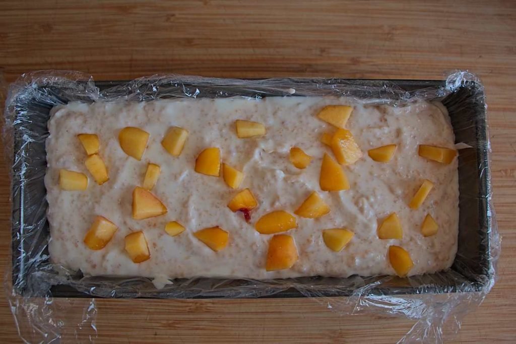 Terrine mixture in a loaf tin topped with diced fresh peaches before freezing.