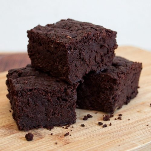 Stack of fudgy vegan tromboncino squash brownies on a wooden board.