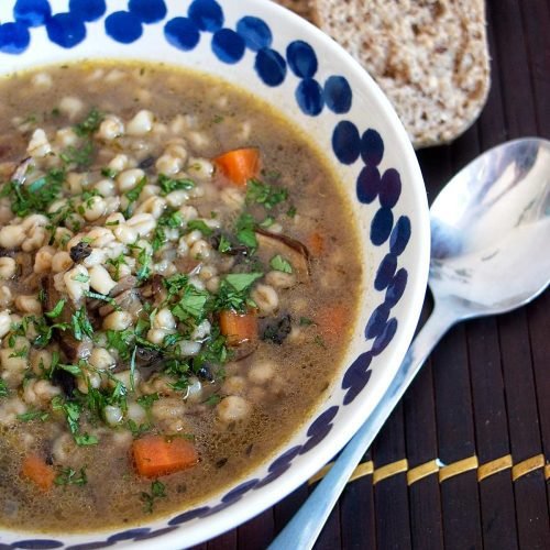 Wheat berry and wild mushroom soup served in a bowl with fresh parsley and bread