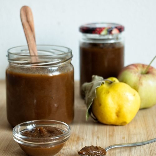 Homemade apple and quince ketchup in a jar with quinces and apples on a wooden board.
