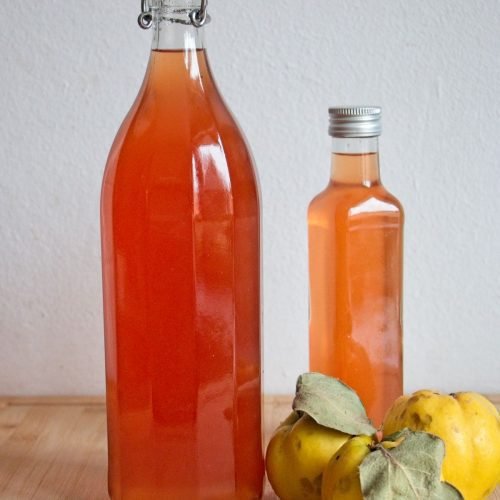 Bottles of homemade quince cordial with fresh quinces on a wooden surface.