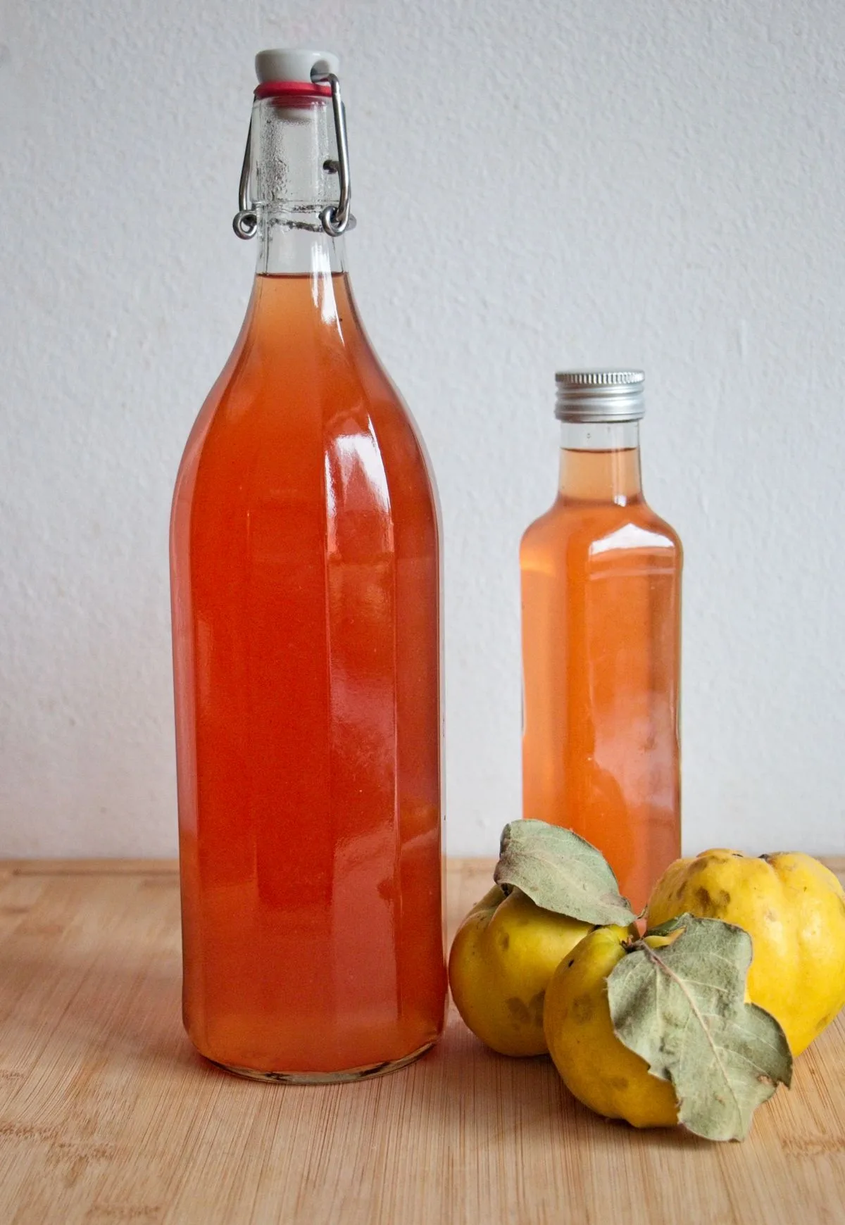 Bottles of homemade quince cordial with fresh quinces on a wooden surface.