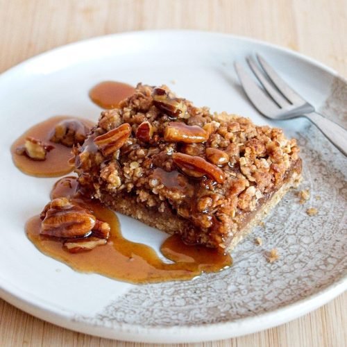 Slice of caramel apple pecan crumble bar on a white plate, drizzled with glossy vegan caramel sauce.