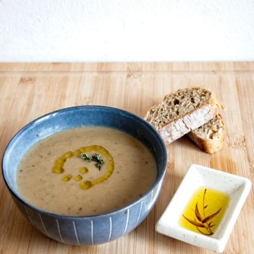 Creamy cep and chestnut soup served in a blue bowl with bread and infused oil on the side.