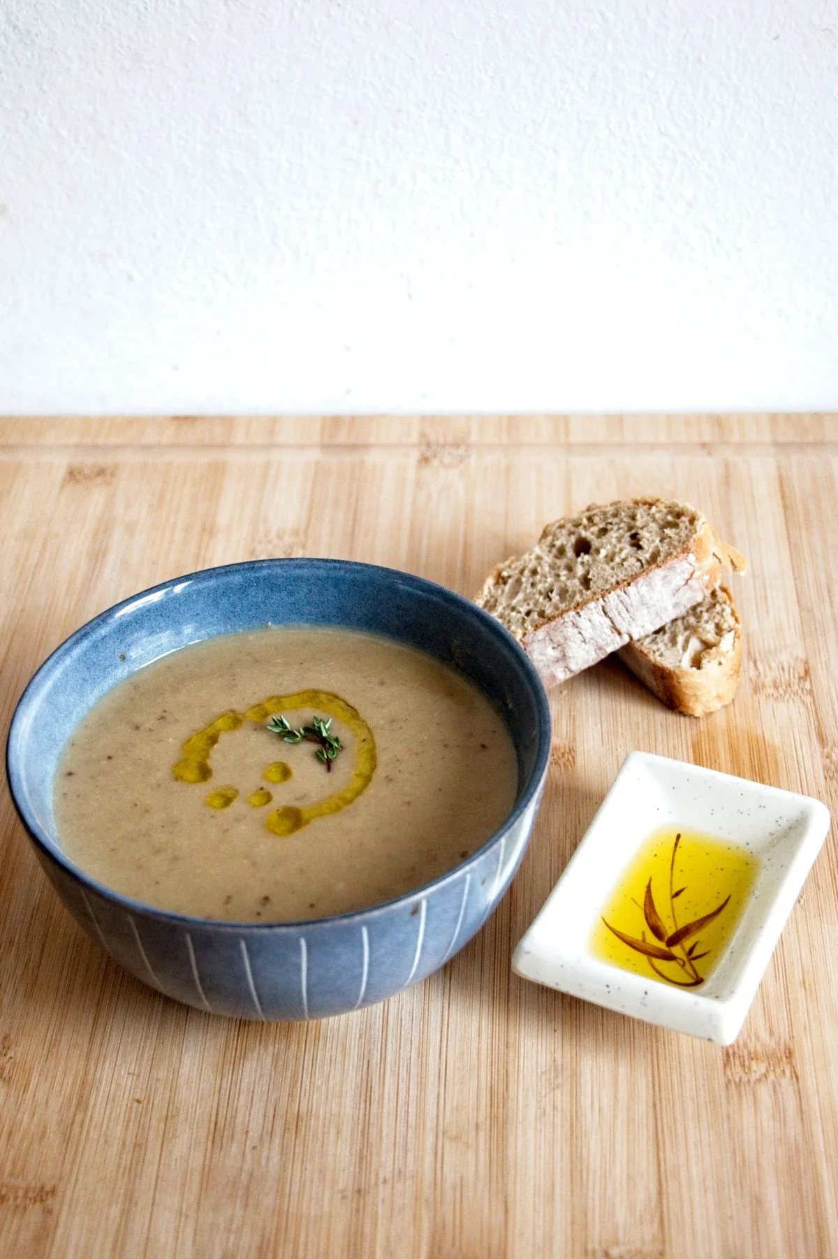 Creamy cep and chestnut soup served in a blue bowl with bread and infused oil on the side.