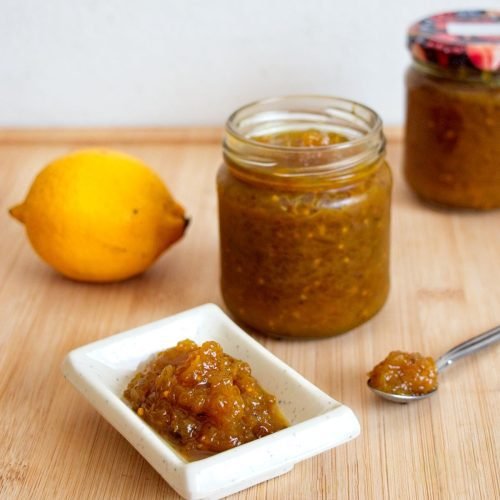 Homemade cucumber chutney in jars with a small serving on a plate and a fresh lemon beside it.