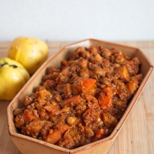 Thick quince and pumpkin stew served in a rustic baking dish with fresh quinces in the background.