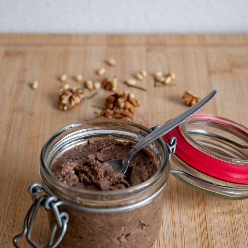 Homemade parasol mushroom pâté in a glass jar with spoon, served on a wooden board with walnuts and pine nuts