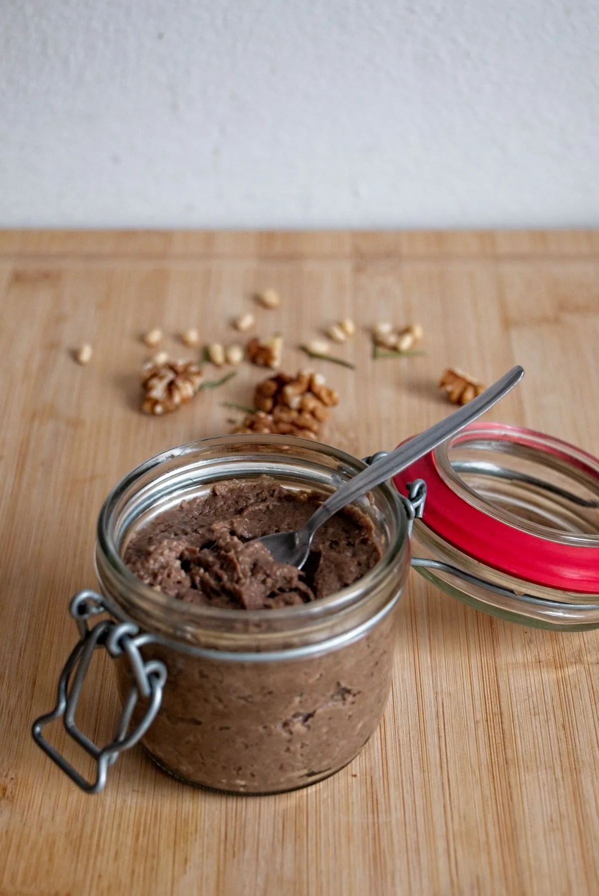 Homemade parasol mushroom pâté in a glass jar with spoon, served on a wooden board with walnuts and pine nuts