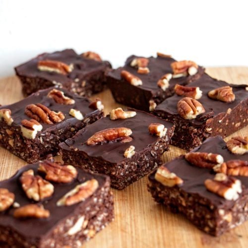Stack of mocha pecan protein bars topped with dark chocolate and toasted pecans on a wooden board.