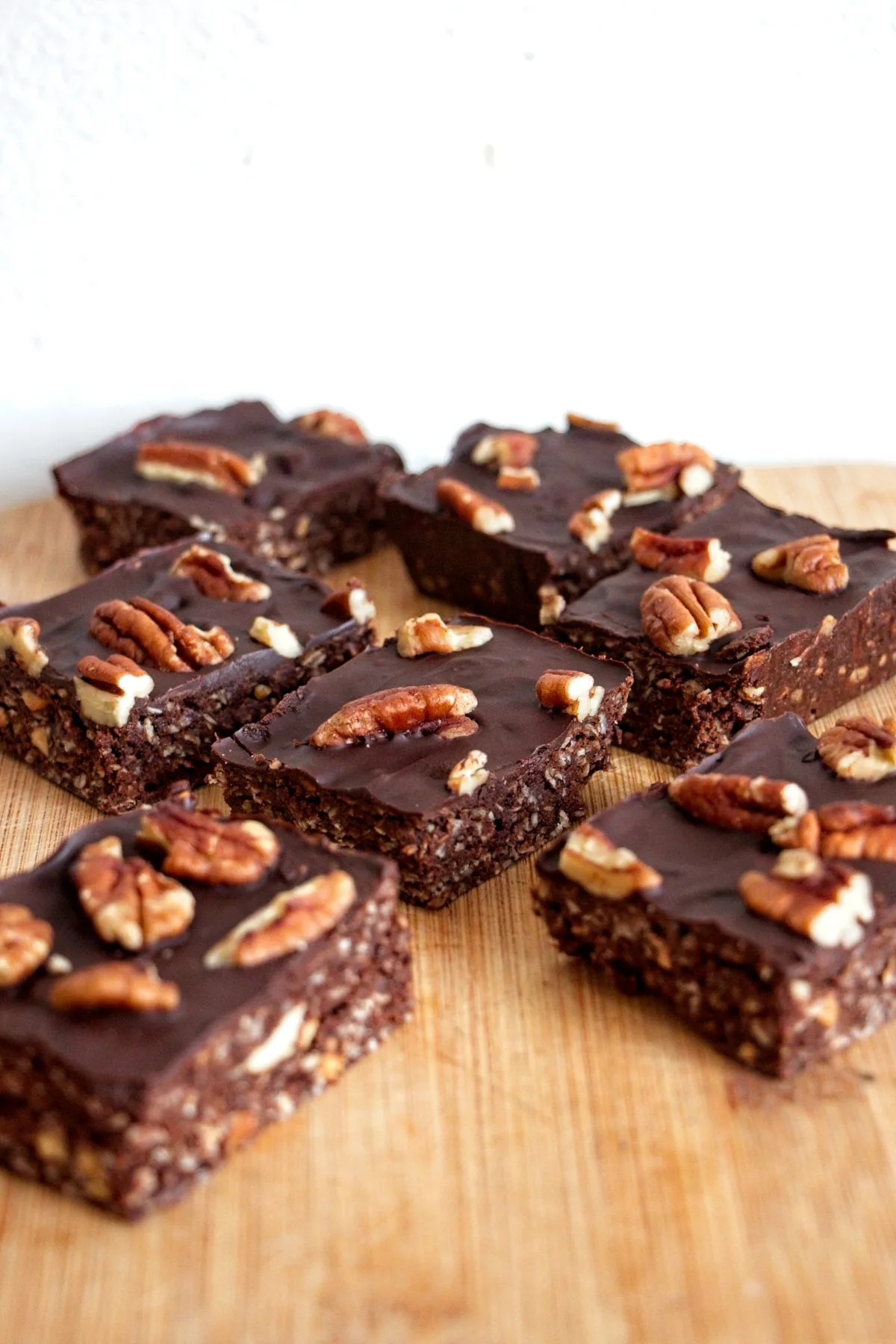 Stack of mocha pecan protein bars topped with dark chocolate and toasted pecans on a wooden board.