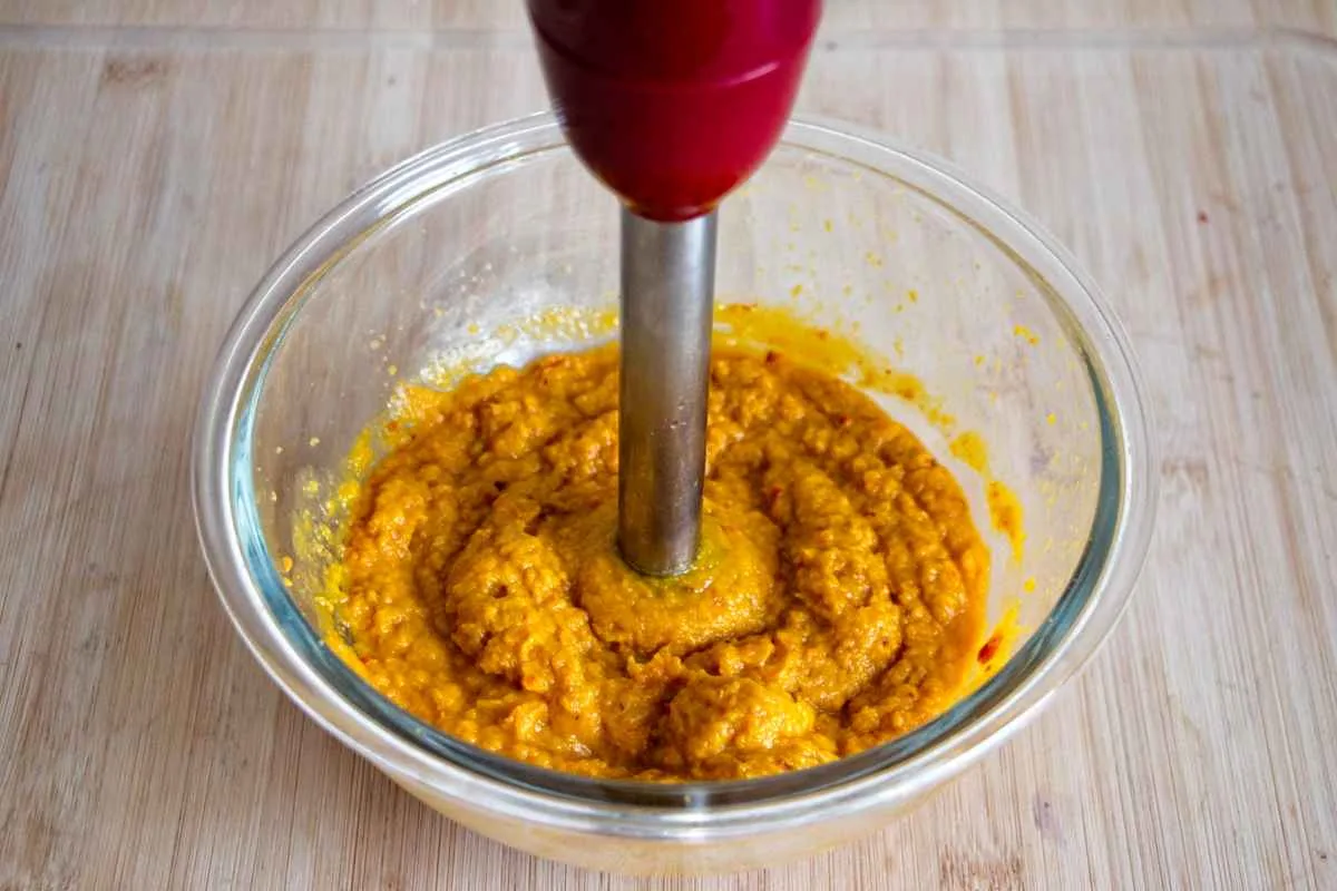 Blending roasted pumpkin in a glass bowl with an immersion blender to make purée.
