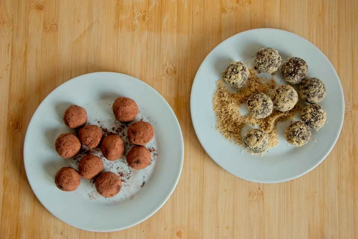 Vegan chestnut truffles on two plates, coated in cocoa and crushed nuts.