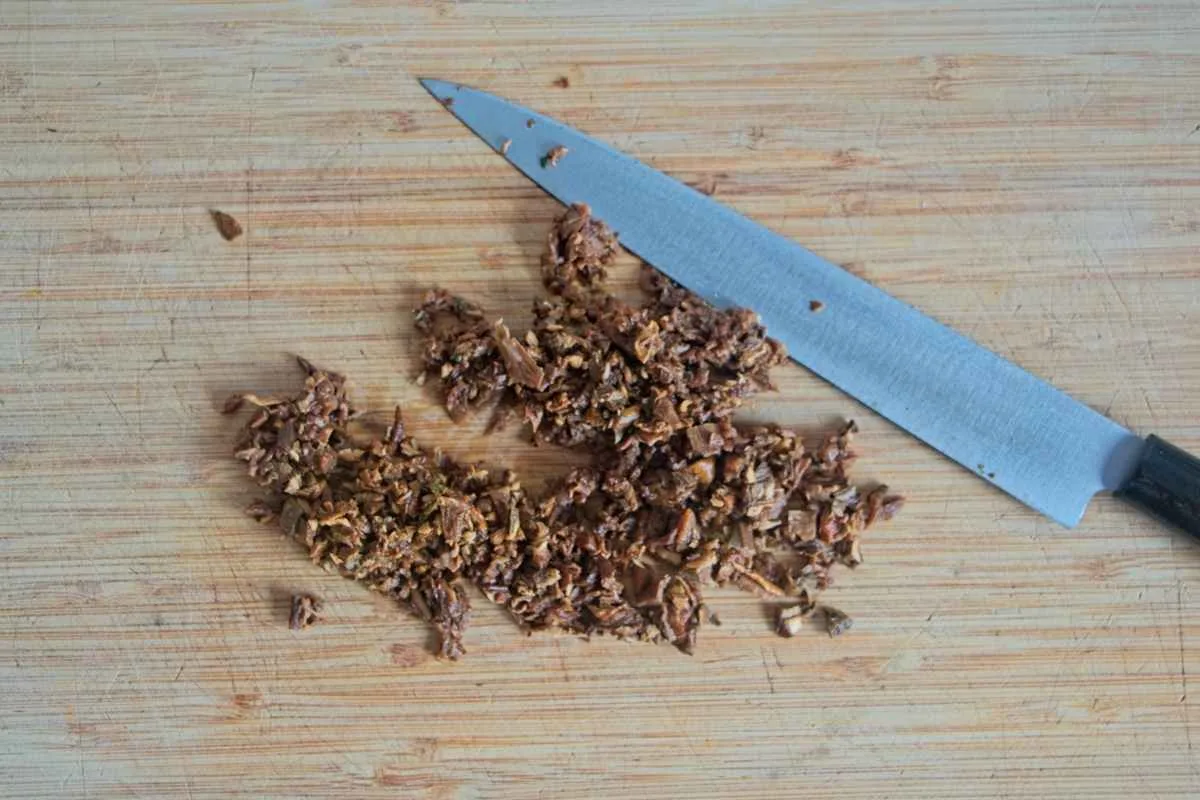 Finely chopped mushrooms on a wooden board with a knife beside them.
