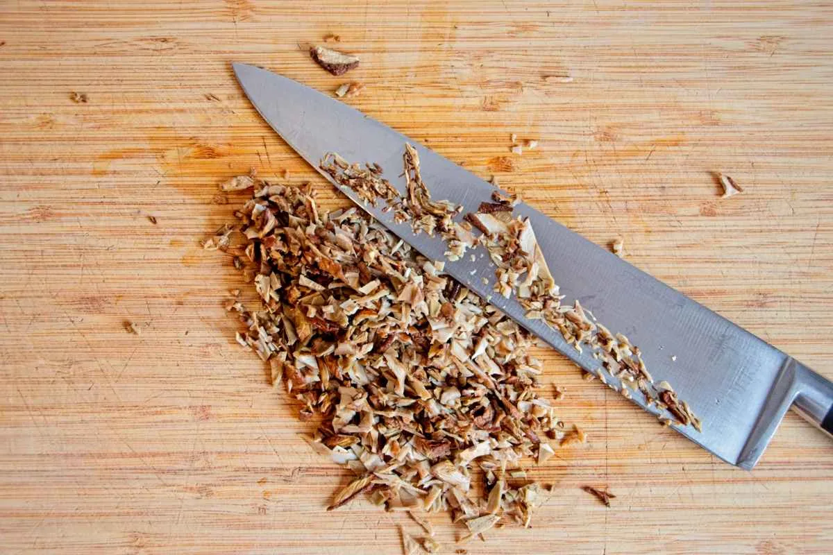 Finely chopping rehydrated ceps on a wooden board with a chef’s knife.