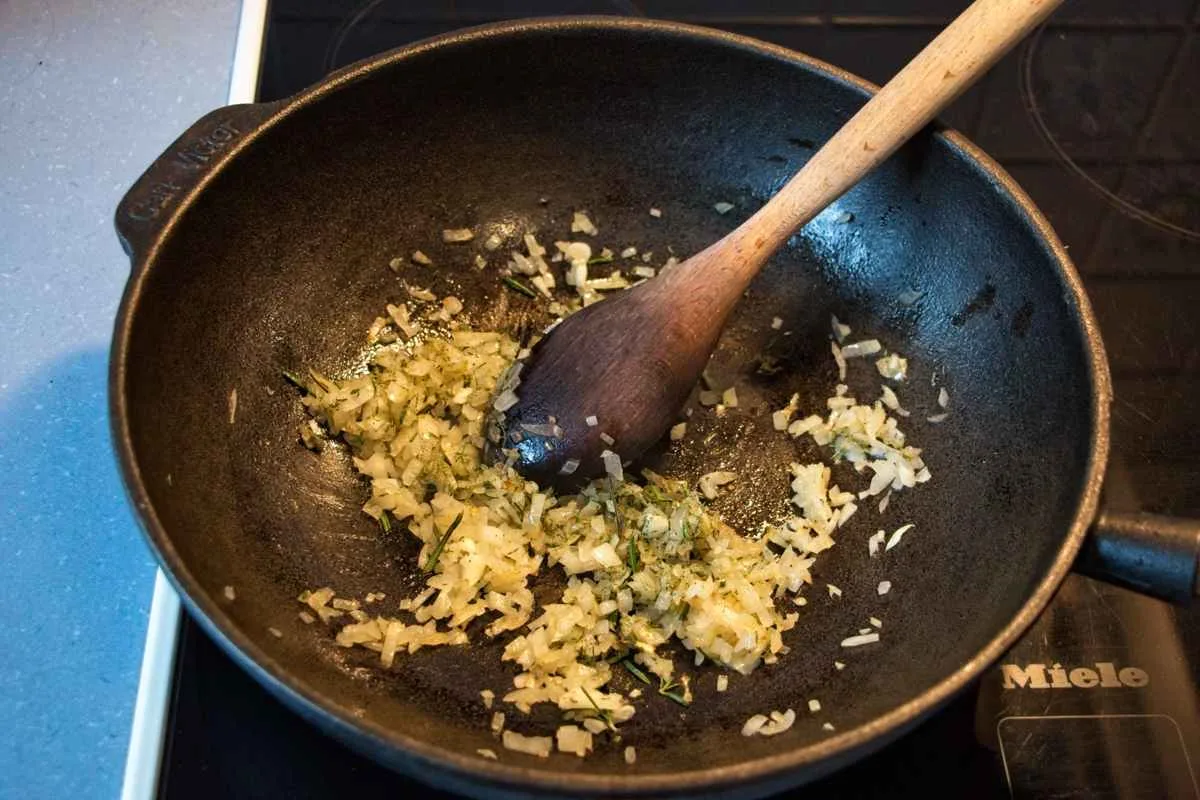 Onions, garlic, and herbs sautéing in a pan before adding flour.