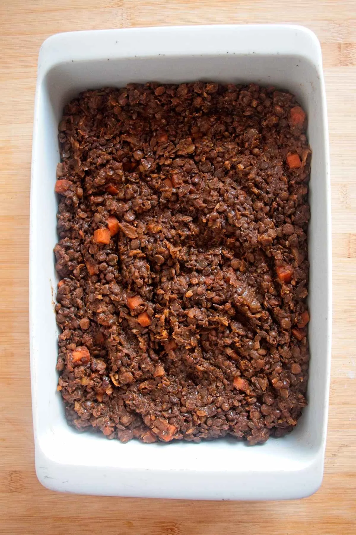 Lentil and vegetable filling spread evenly in a white baking dish before adding the mash.