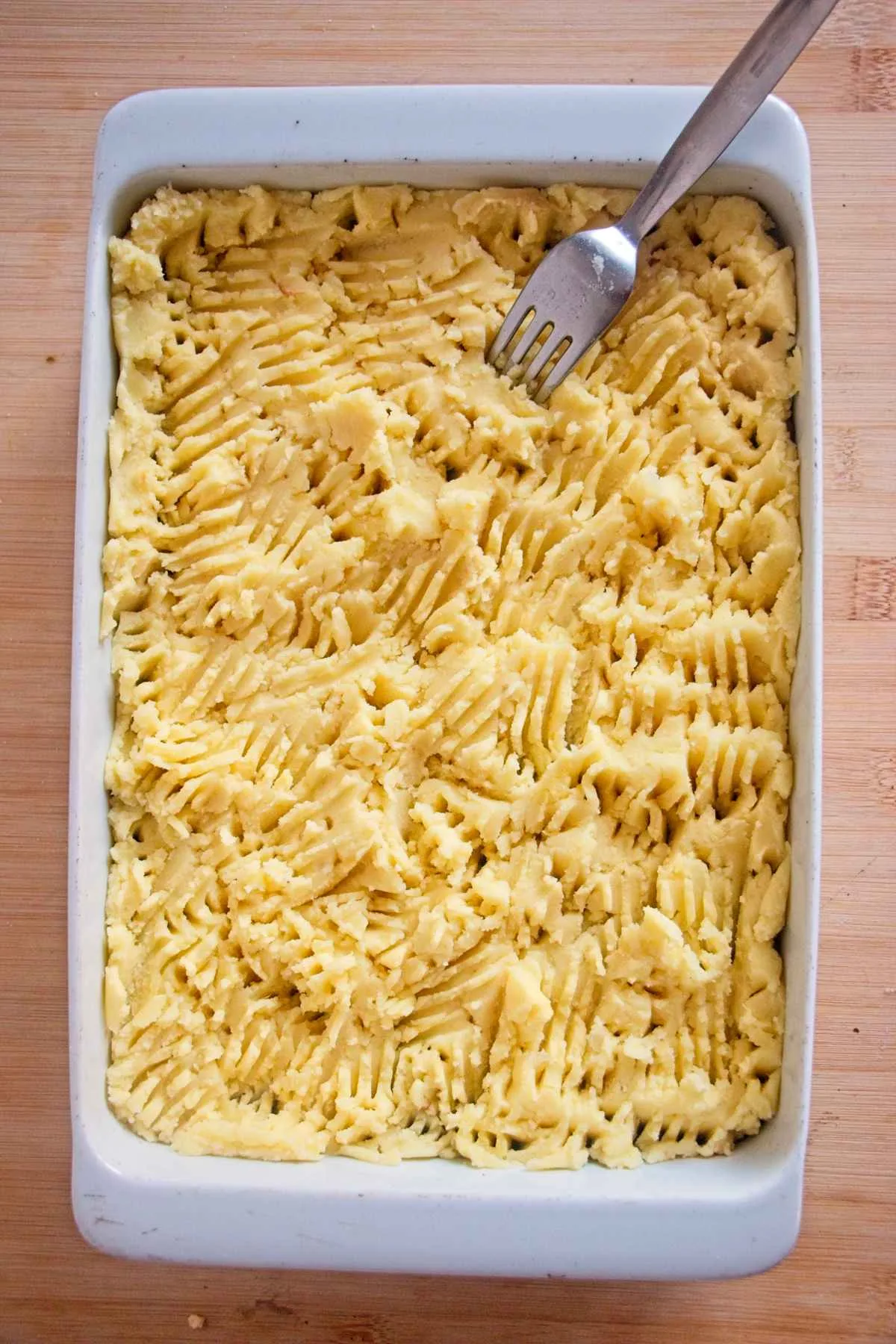 Mashed potato topping in a baking dish being textured with a fork.