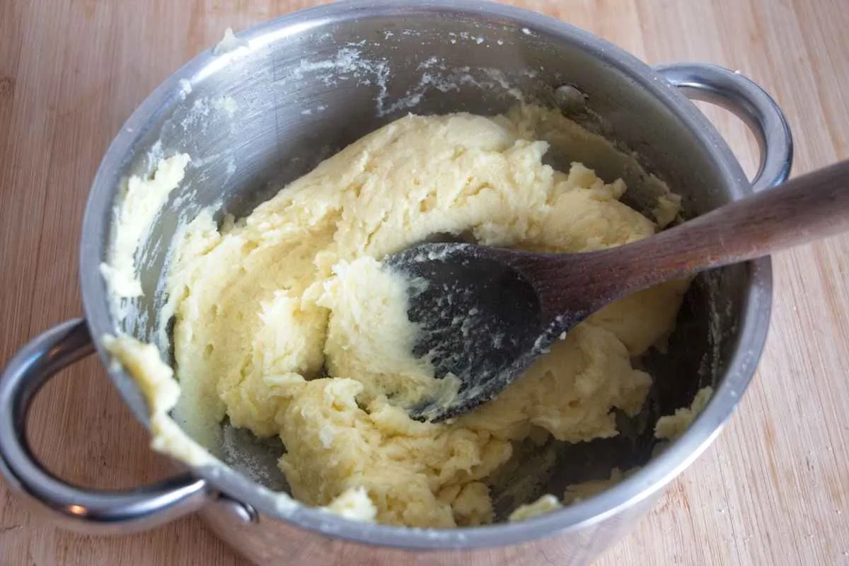 Mashed potato mixed with butter and milk in a saucepan with a wooden spoon.