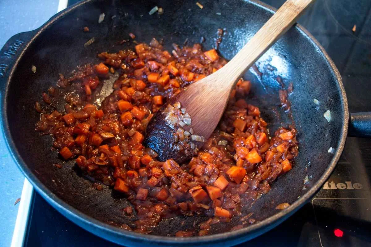 Carrot and onion mixture in a pan after deglazing, stirred with a wooden spoon.
