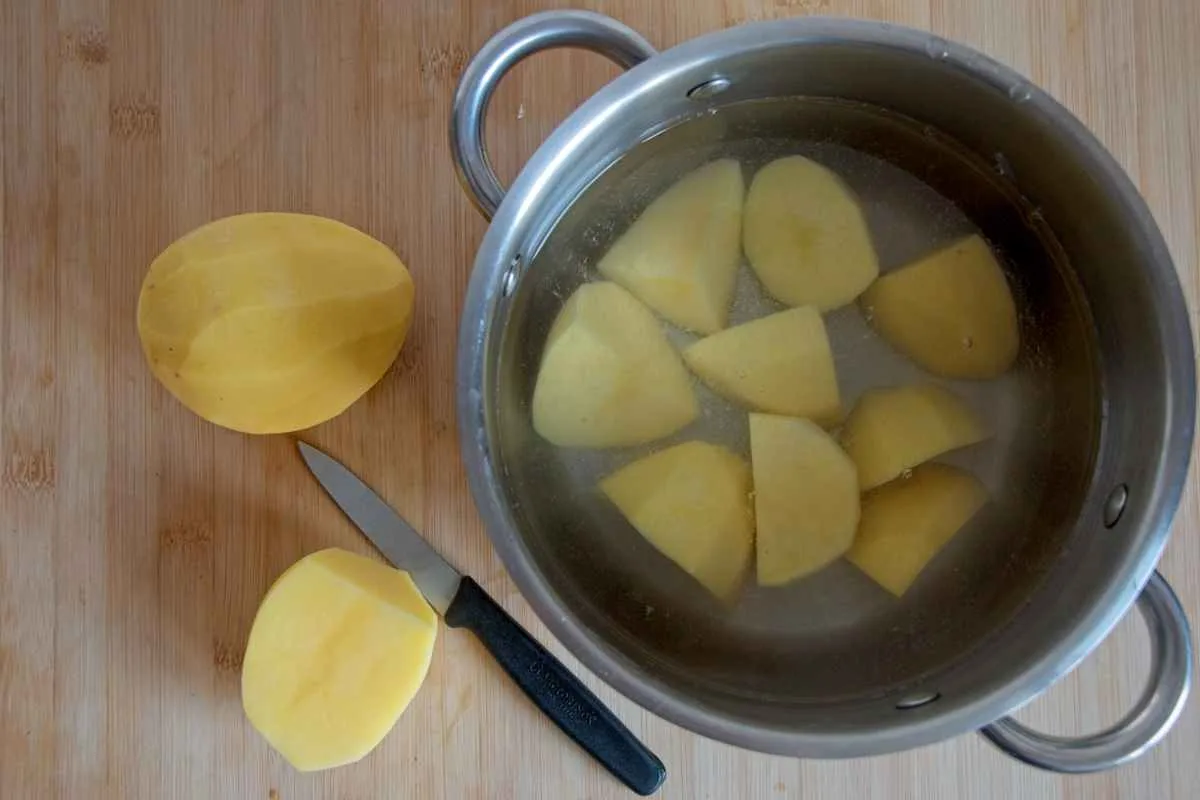 Peeled and chopped potatoes in a pot of water with a knife on a wooden board.